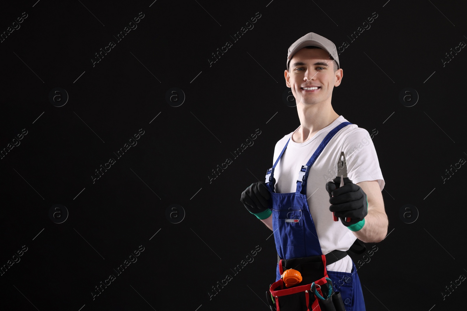 Photo of Young man holding pliers on black background, space for text