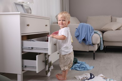 Photo of Cute little boy playing with clothes in dresser's drawer at home