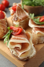 Photo of Tasty sandwiches with cured ham, tomatoes and arugula on wooden board, closeup