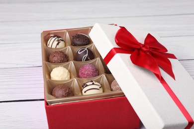 Photo of Red box with tasty chocolate candies on white wooden table, closeup