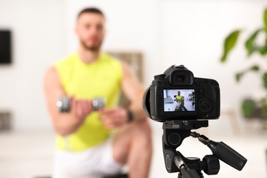 Photo of Trainer with dumbbell recording workout at home, focus on camera. Space for text
