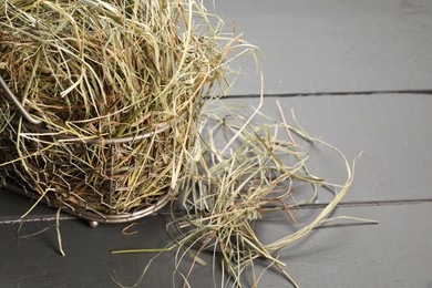 Photo of Dried hay in metal basket on grey wooden table, closeup. Space for text