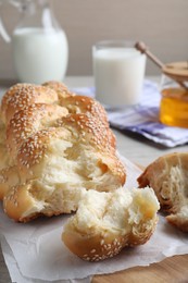 Photo of Broken homemade braided bread with sesame seeds on wooden table, closeup. Traditional Shabbat challah