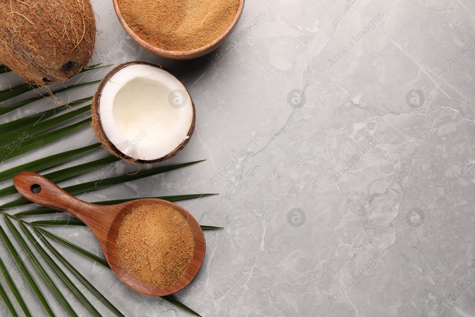 Photo of Spoon with coconut sugar, palm leaves, bowl and fruit on grey marble table, flat lay. Space for text