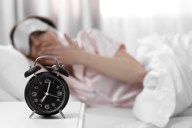 Photo of Young woman at home in morning, focus on alarm clock. Space for text
