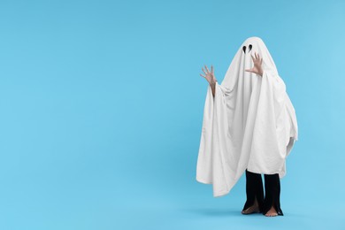 Woman in white ghost costume on light blue background, space for text. Halloween celebration
