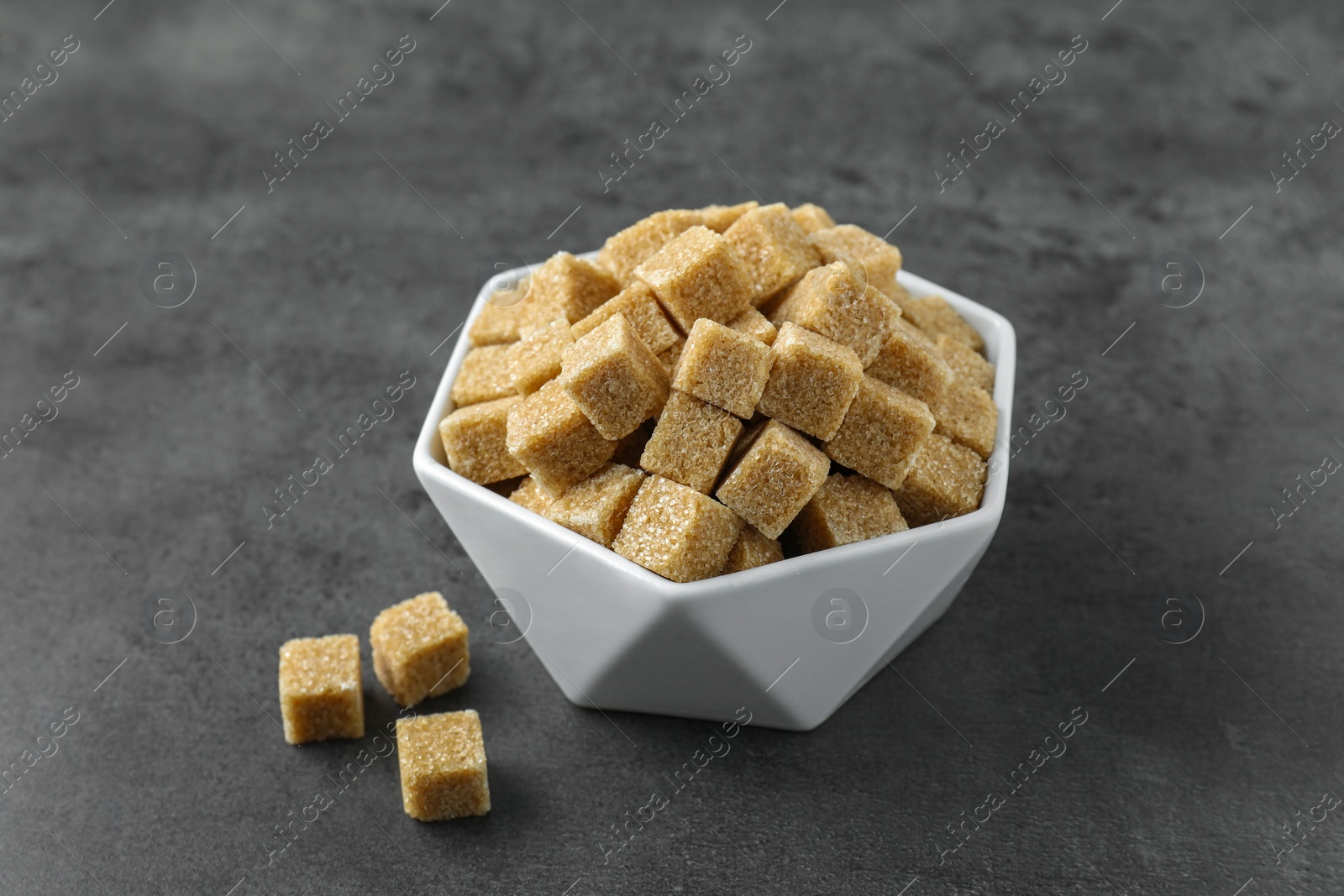 Photo of Brown sugar cubes in bowl on grey table