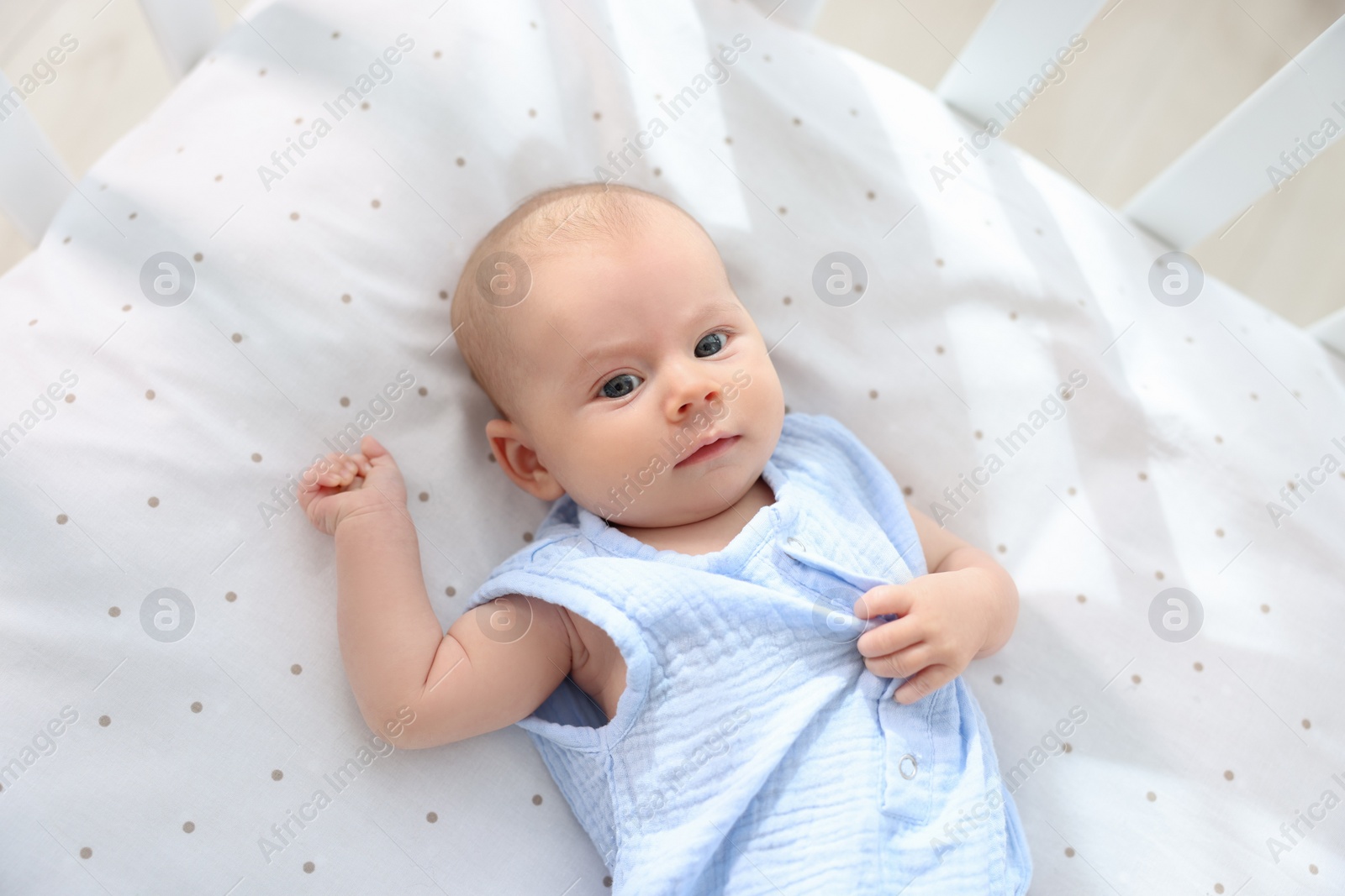 Photo of Cute little baby lying in crib at home, top view