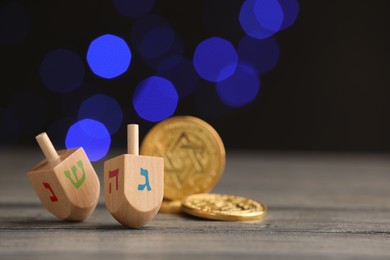 Photo of Dreidels with Jewish letters and coins on wooden table against blurred festive lights, selective focus. Space for text. Traditional Hanukkah game