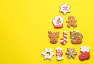 Photo of Delicious gingerbread cookies arranged in shape of Christmas tree on yellow background, flat lay. Space for text