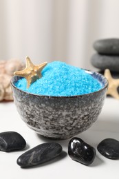 Photo of Light blue sea salt in bowl, spa stones and starfish on white table