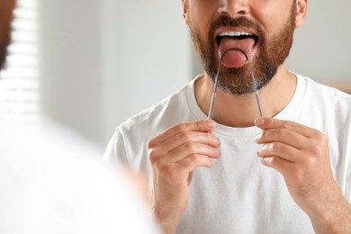 Man brushing his tongue with cleaner near mirror in bathroom, closeup