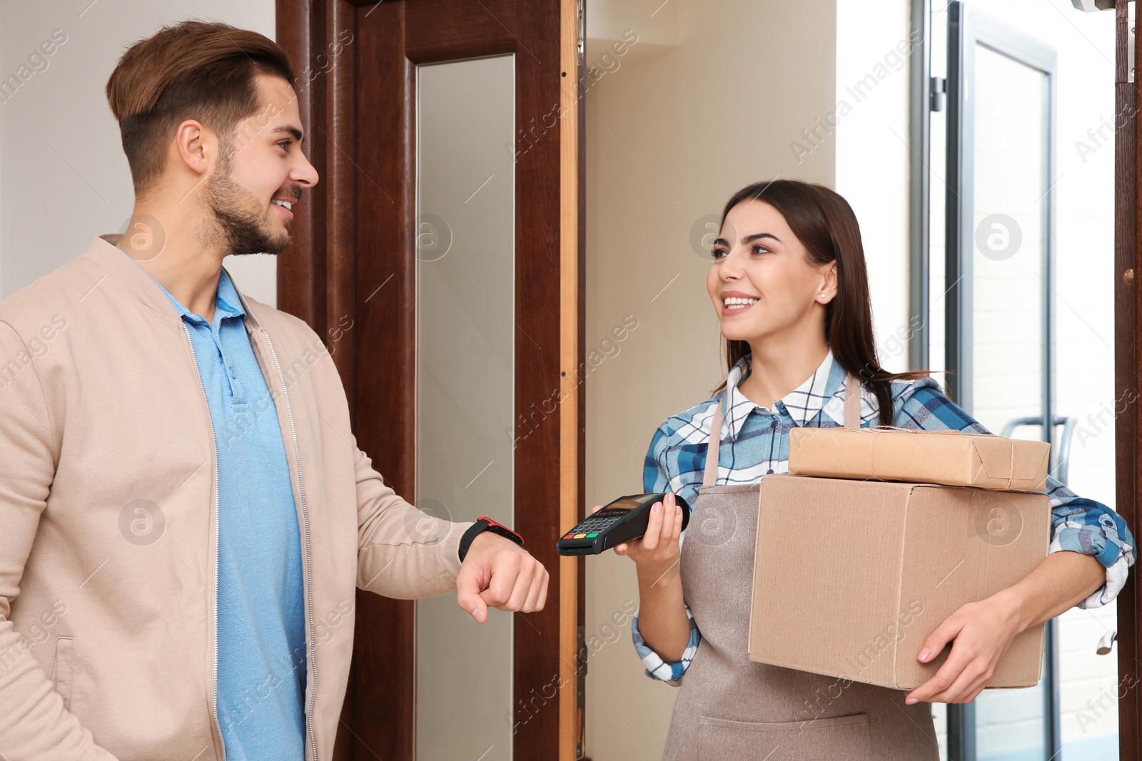 Photo of Young man with smartwatch using terminal for delivery payment indoors