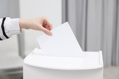 Photo of Woman putting her vote into ballot box on blurred background, closeup