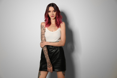 Beautiful woman with tattoos on body against light background