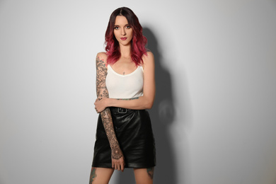 Photo of Beautiful woman with tattoos on body against light background