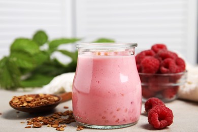 Photo of Tasty raspberry smoothie with granola in glass jar and fresh berries on light table, closeup