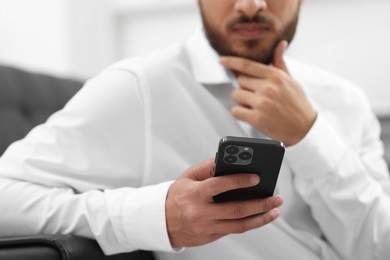 Photo of Young man using smartphone indoors, selective focus