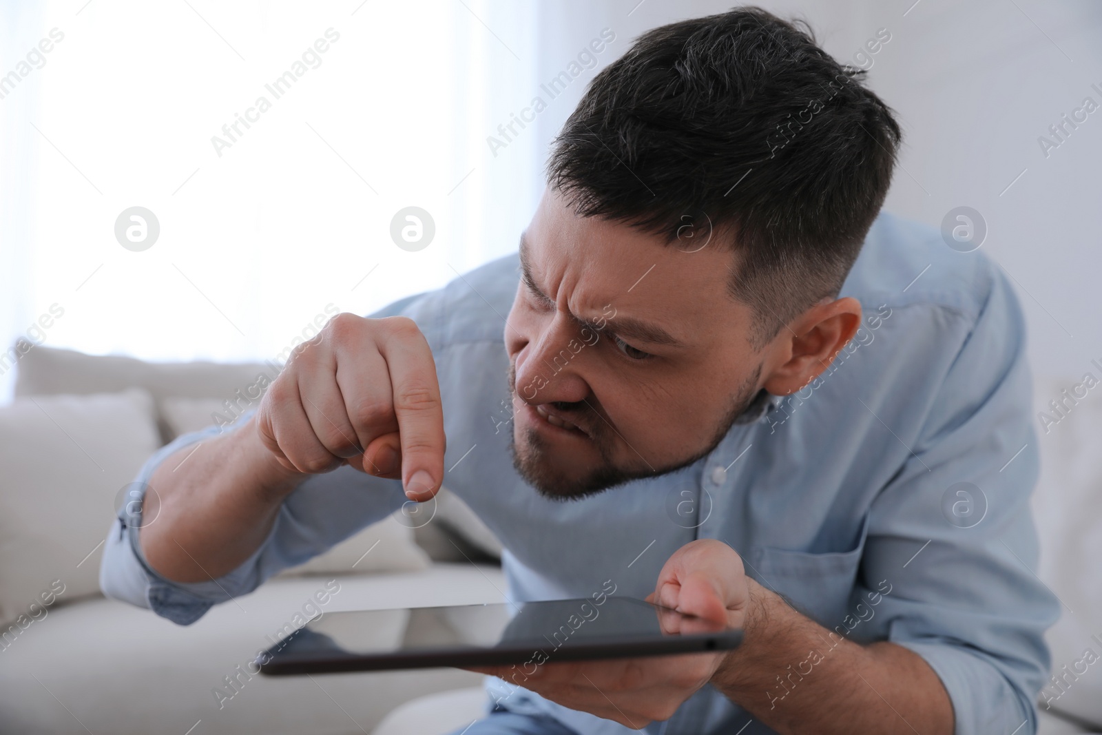 Photo of Emotional man with tablet at home. Online hate concept