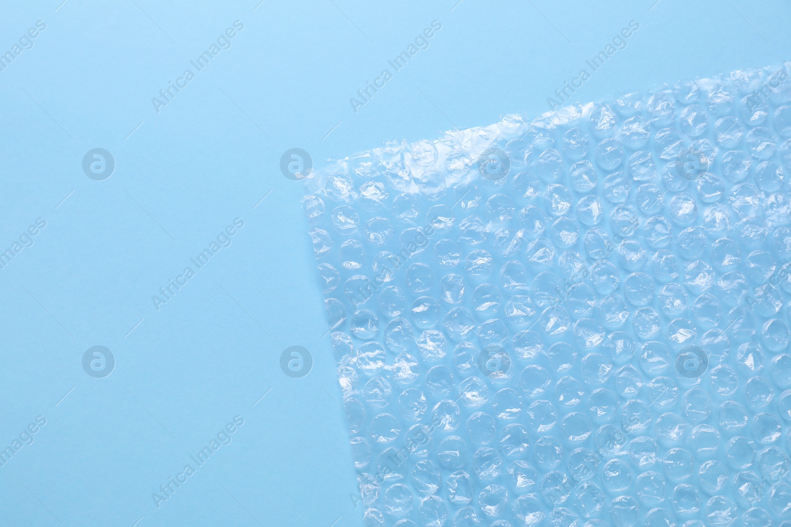 Photo of Transparent bubble wrap on light blue background, top view. Space for text