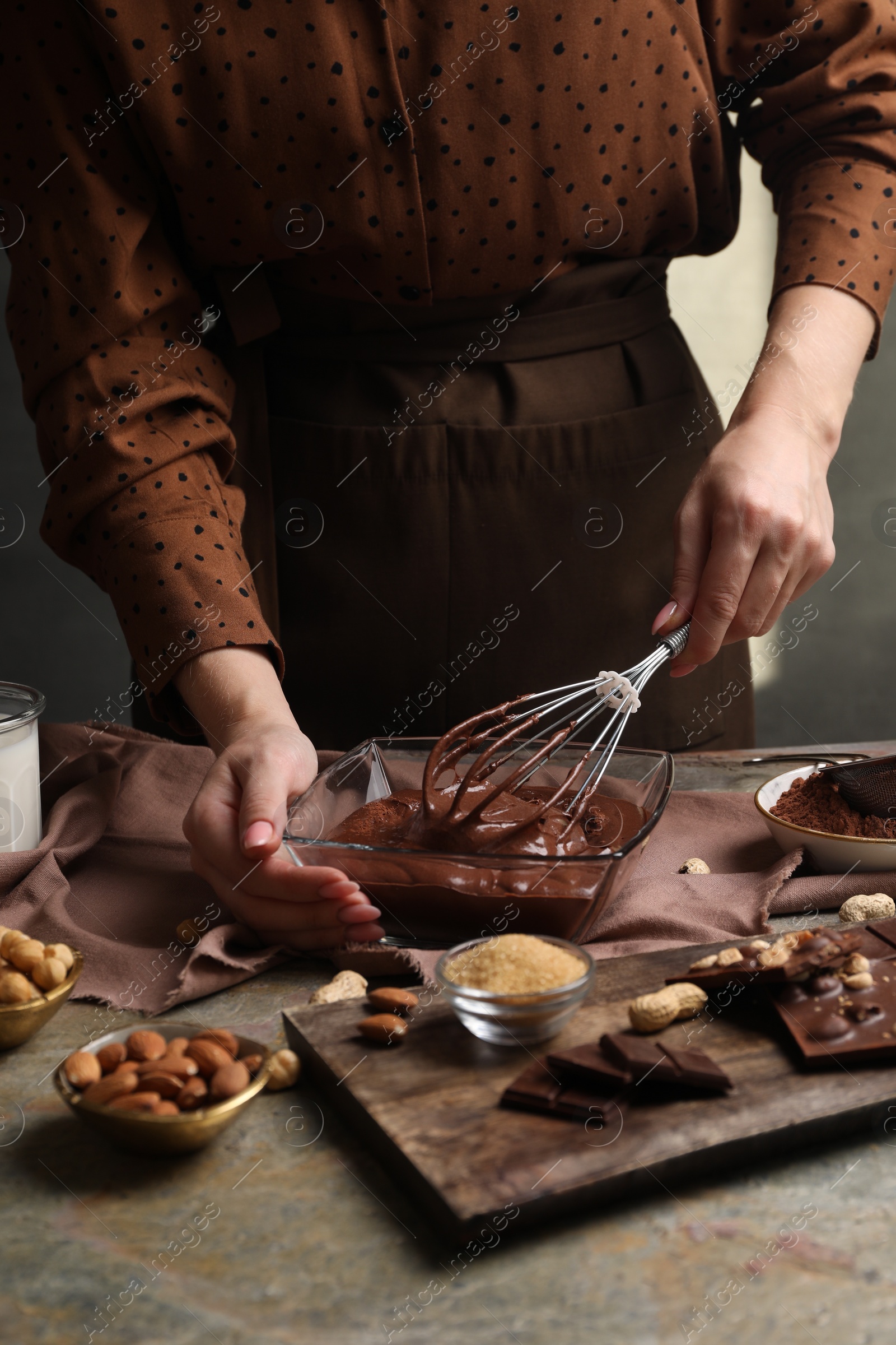 Photo of Woman mixing delicious chocolate cream with whisk at grey textured table, closeup