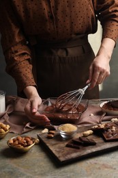 Photo of Woman mixing delicious chocolate cream with whisk at grey textured table, closeup