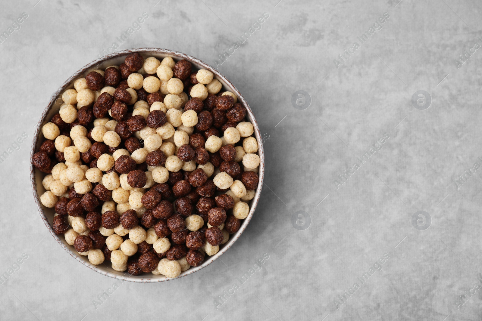 Photo of Tasty cereal balls in bowl on grey table, top view. Space for text