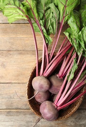Raw ripe beets in wicker bowl on wooden table, top view