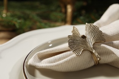 Photo of White fabric napkin with beautiful decorative ring for table setting on plate, closeup