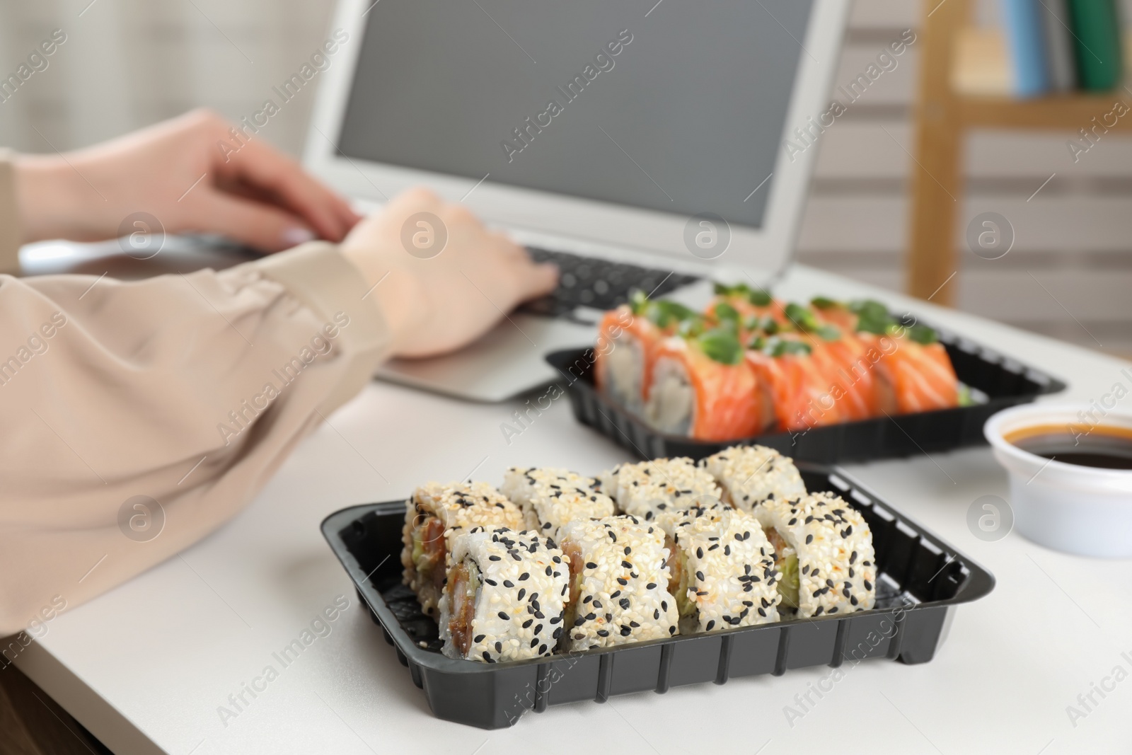 Photo of Woman using laptop in office, focus on tasty sushi rolls. Lunch break at work