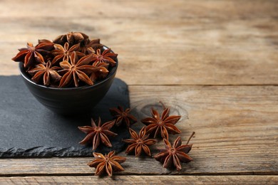Photo of Aromatic anise stars with bowl on wooden table. Space for text