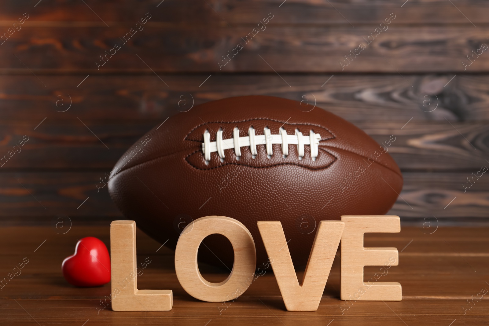 Photo of American football ball, heart and word Love on wooden table