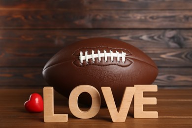 Photo of American football ball, heart and word Love on wooden table