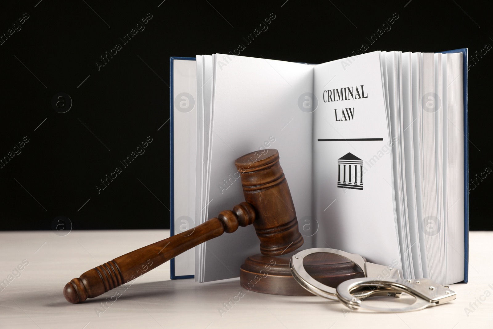 Photo of Judge's gavel, handcuffs and Criminal law book on white table against black background