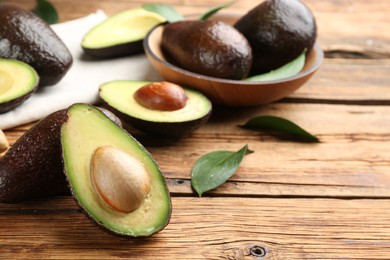 Photo of Whole and cut avocados with green leaves on wooden table. Space for text