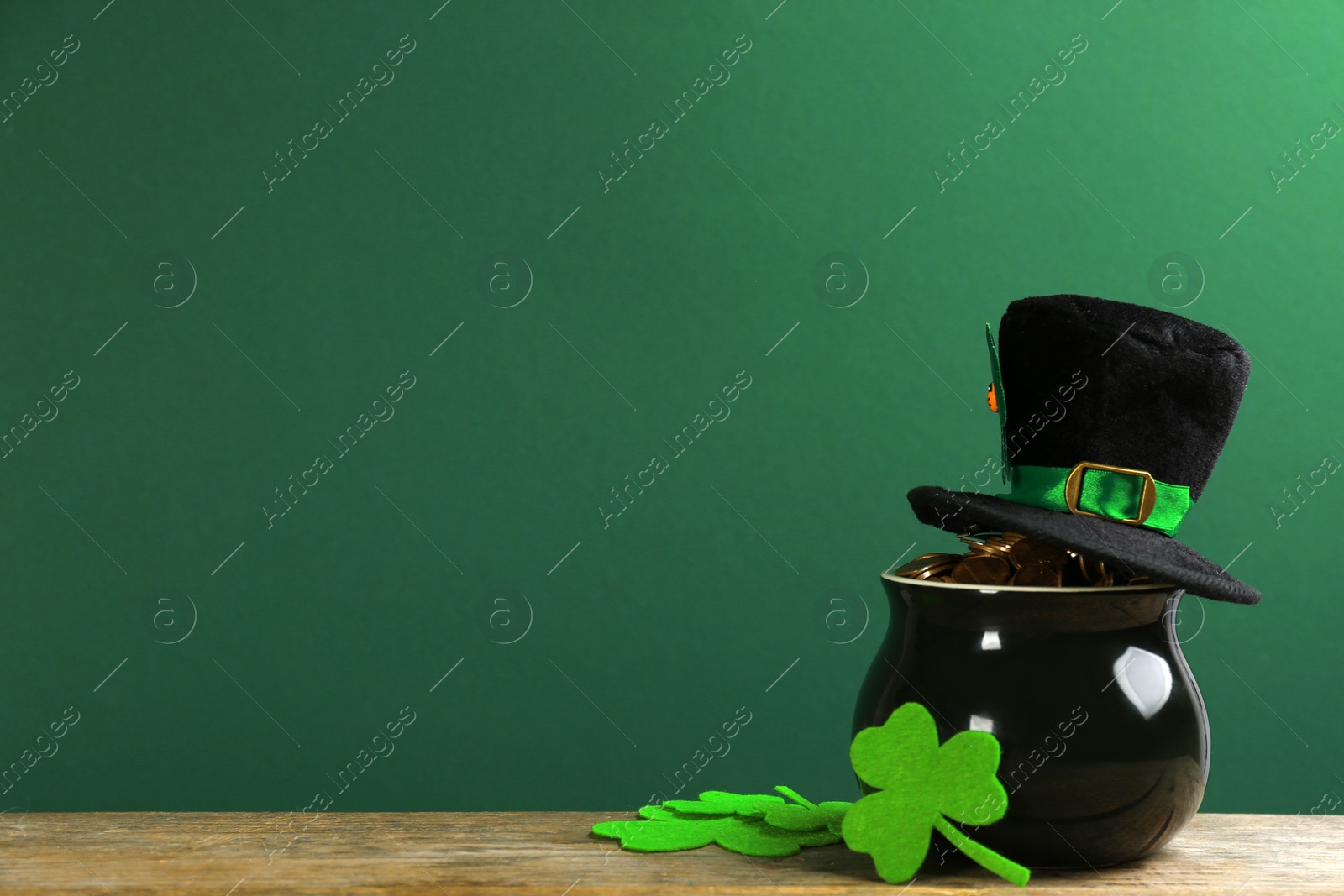 Photo of Pot of gold coins, hat and clover leaves on wooden table against green background, space for text. St. Patrick's Day celebration