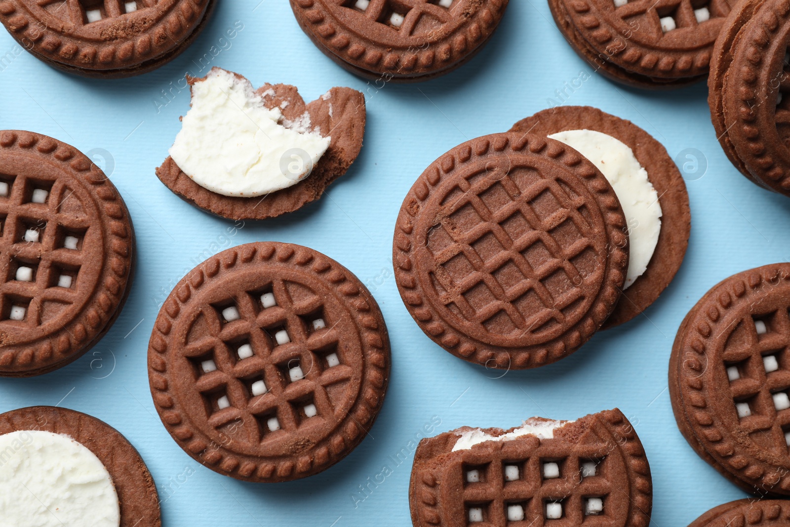 Photo of Tasty chocolate sandwich cookies with cream on light blue background, flat lay