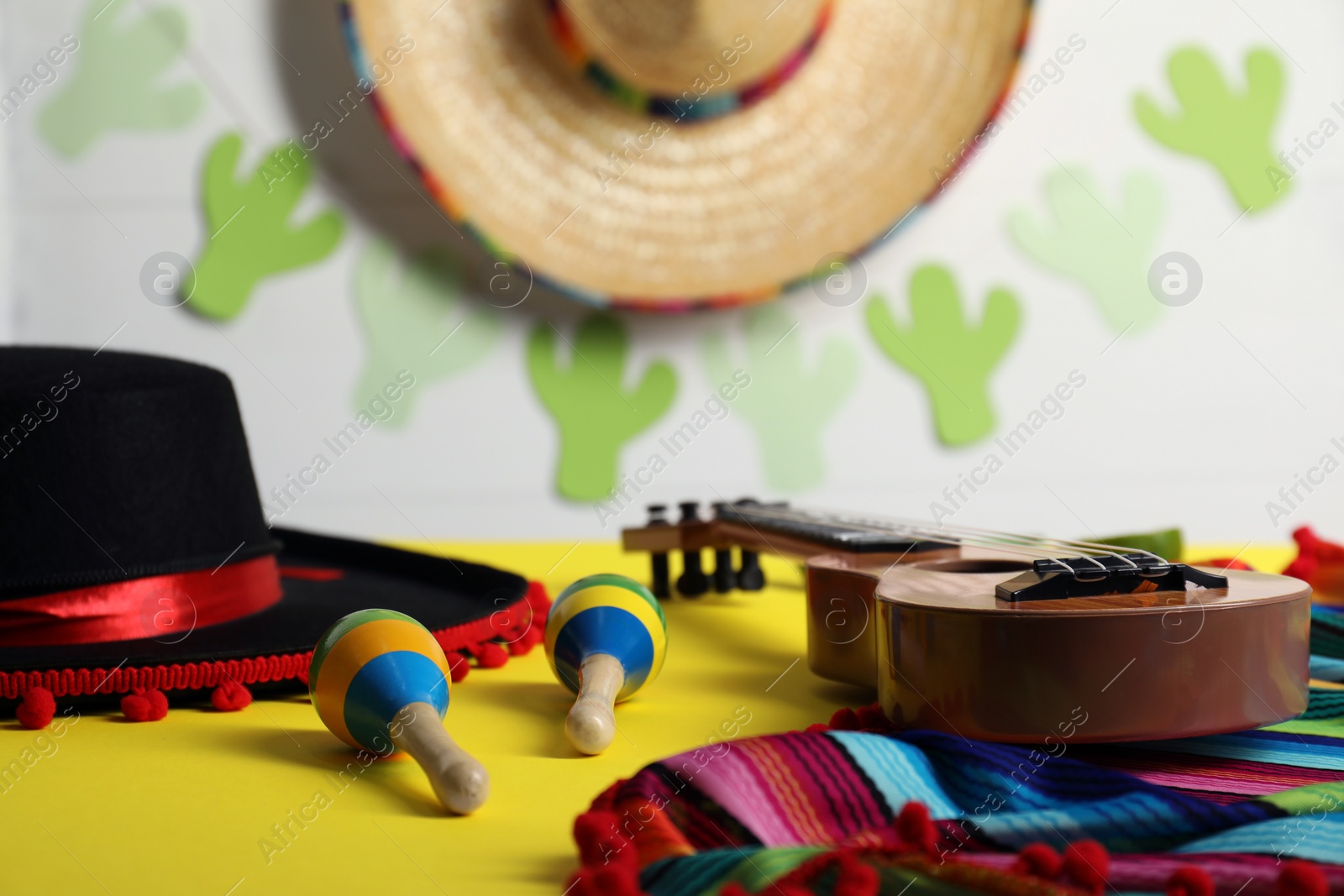 Photo of Black Flamenco hat, poncho, ukulele and maracas on yellow table, closeup