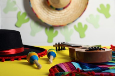 Black Flamenco hat, poncho, ukulele and maracas on yellow table, closeup
