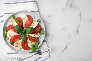 Photo of Caprese salad with tomatoes, mozzarella, basil and spices served on white marble table, top view. Space for text