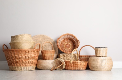 Photo of Many different wicker baskets made of natural material on floor near light wall