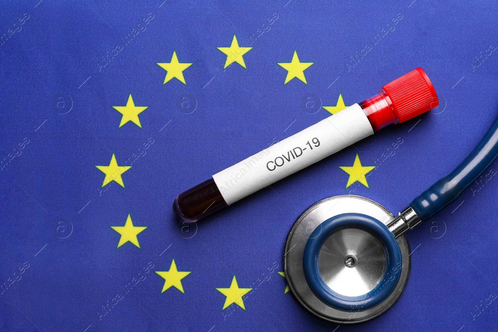 Photo of Stethoscope and test tube with blood sample on European Union flag background, flat lay. Coronavirus outbreak