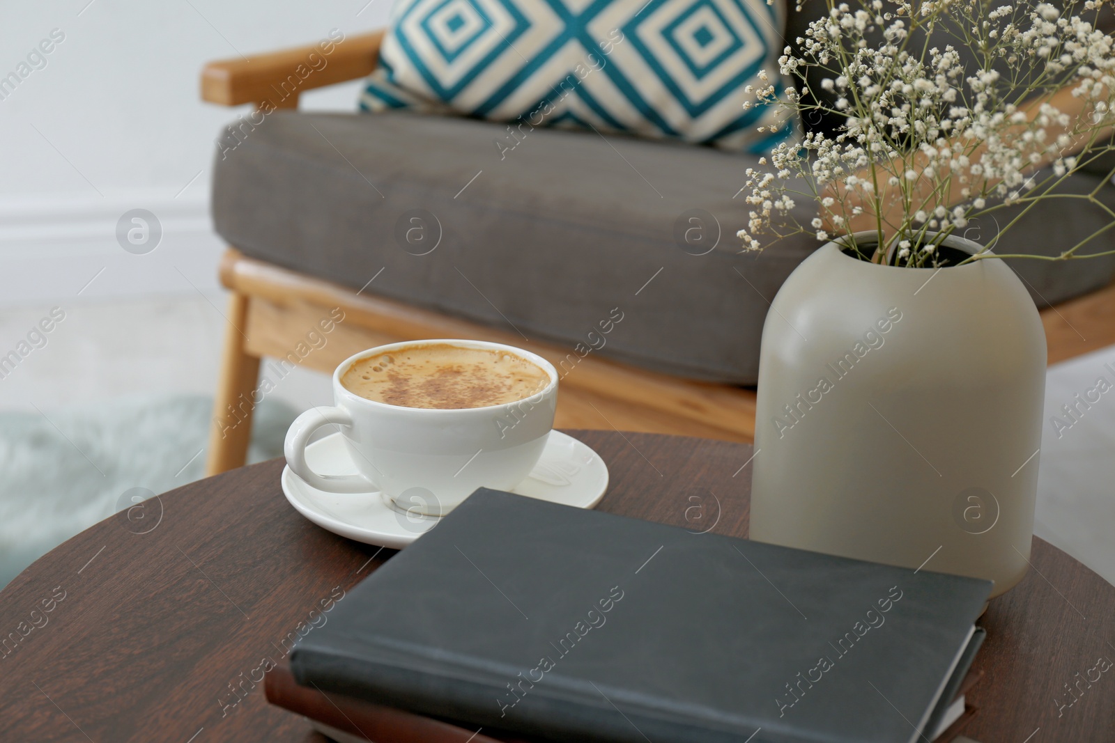 Photo of Cup of coffee and vase with flowers on wooden table in modern living room interior