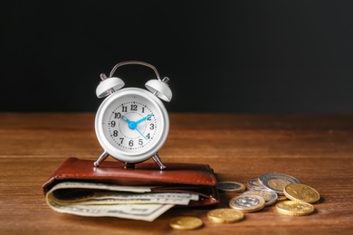 Wallet with banknotes, coins and alarm clock on wooden table. Pension planning