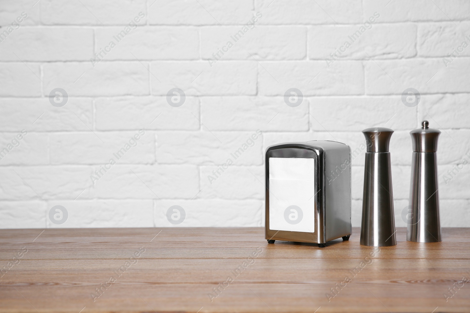 Photo of Napkin holder with salt and pepper shakers on table against brick wall. Space for text