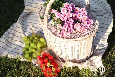 Photo of Picnic basket, flowers and berries on blanket outdoors