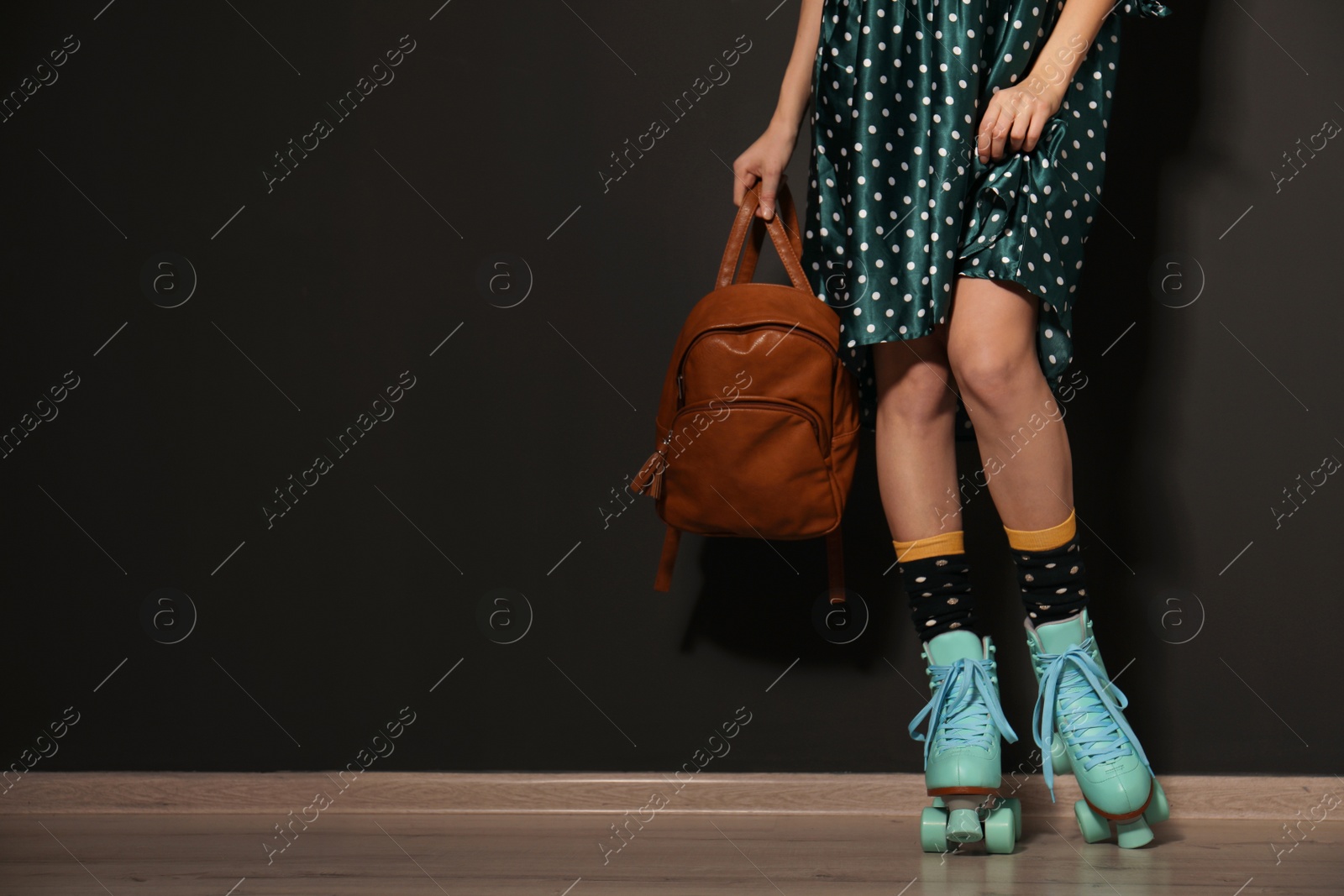 Photo of Young woman with retro roller skates against black wall, closeup. Space for text