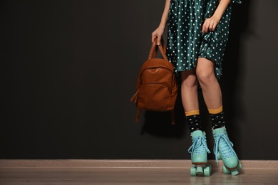 Photo of Young woman with retro roller skates against black wall, closeup. Space for text