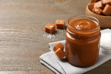 Photo of Yummy salted caramel in glass jar and candies on wooden table, space for text