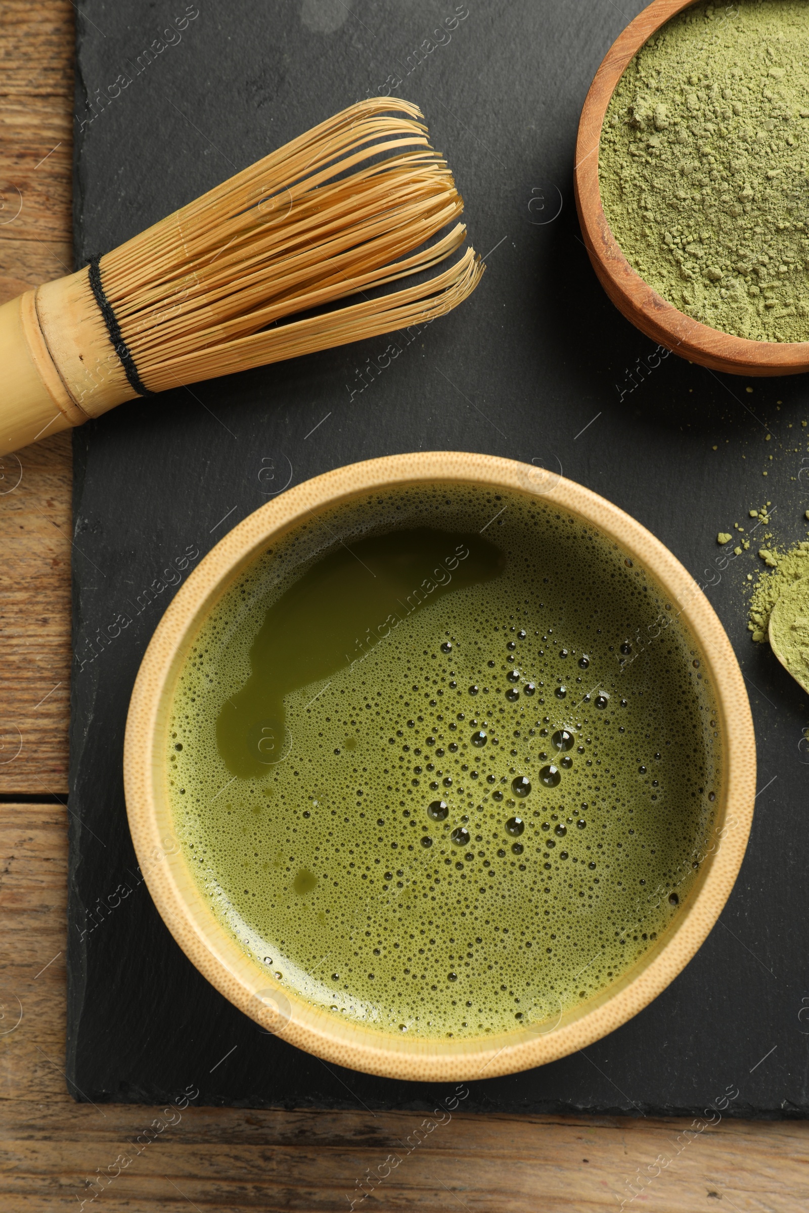 Photo of Cup of fresh matcha tea, green powder and bamboo whisk on wooden table, top view